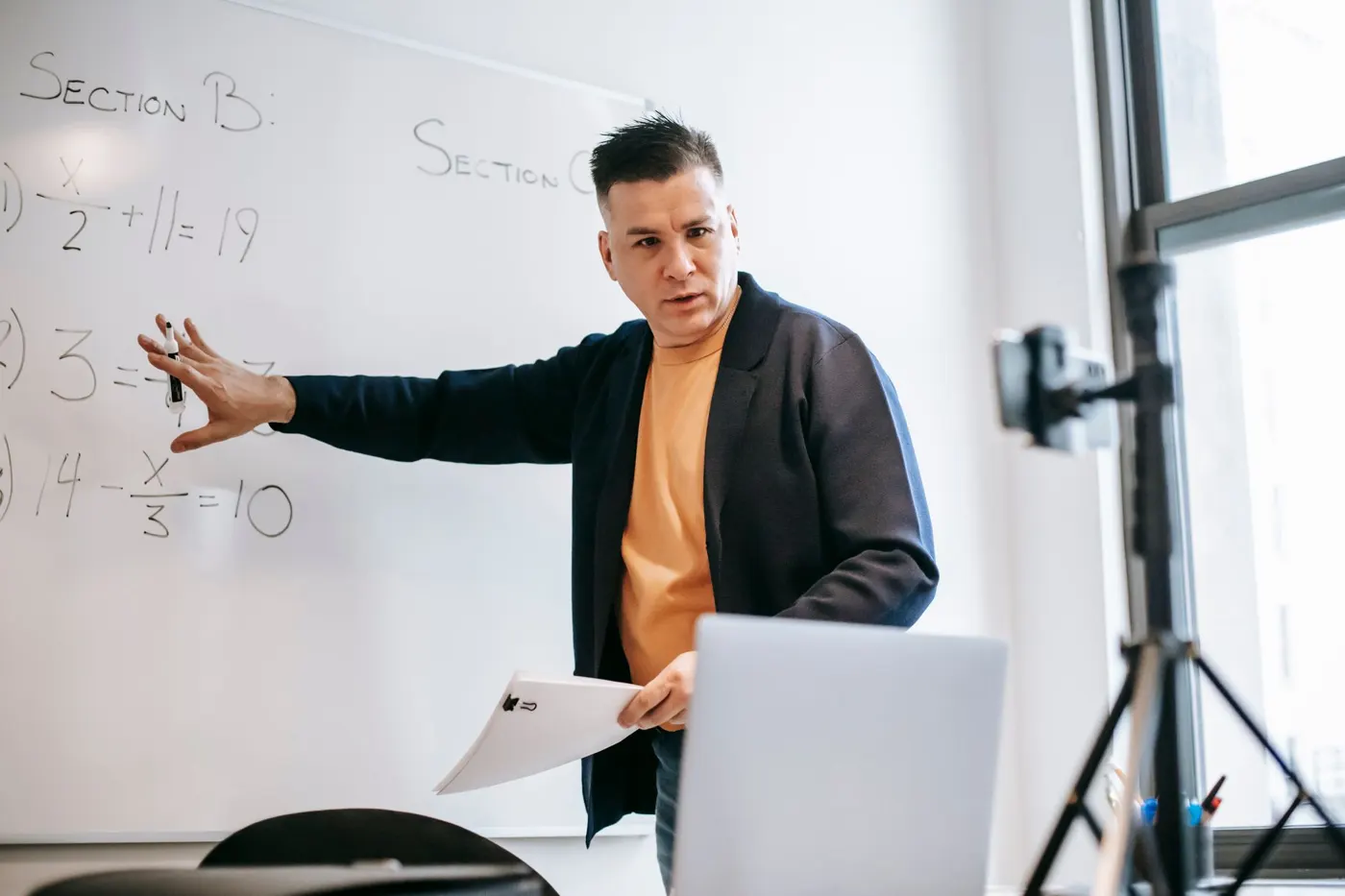 A teacher in front of a whiteboard, teaching to a laptop